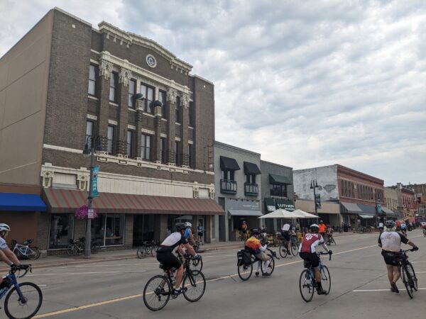 Cyclicts riding past a four story brown brick early 20th Century former Masonic Lodge among other downtown buildings