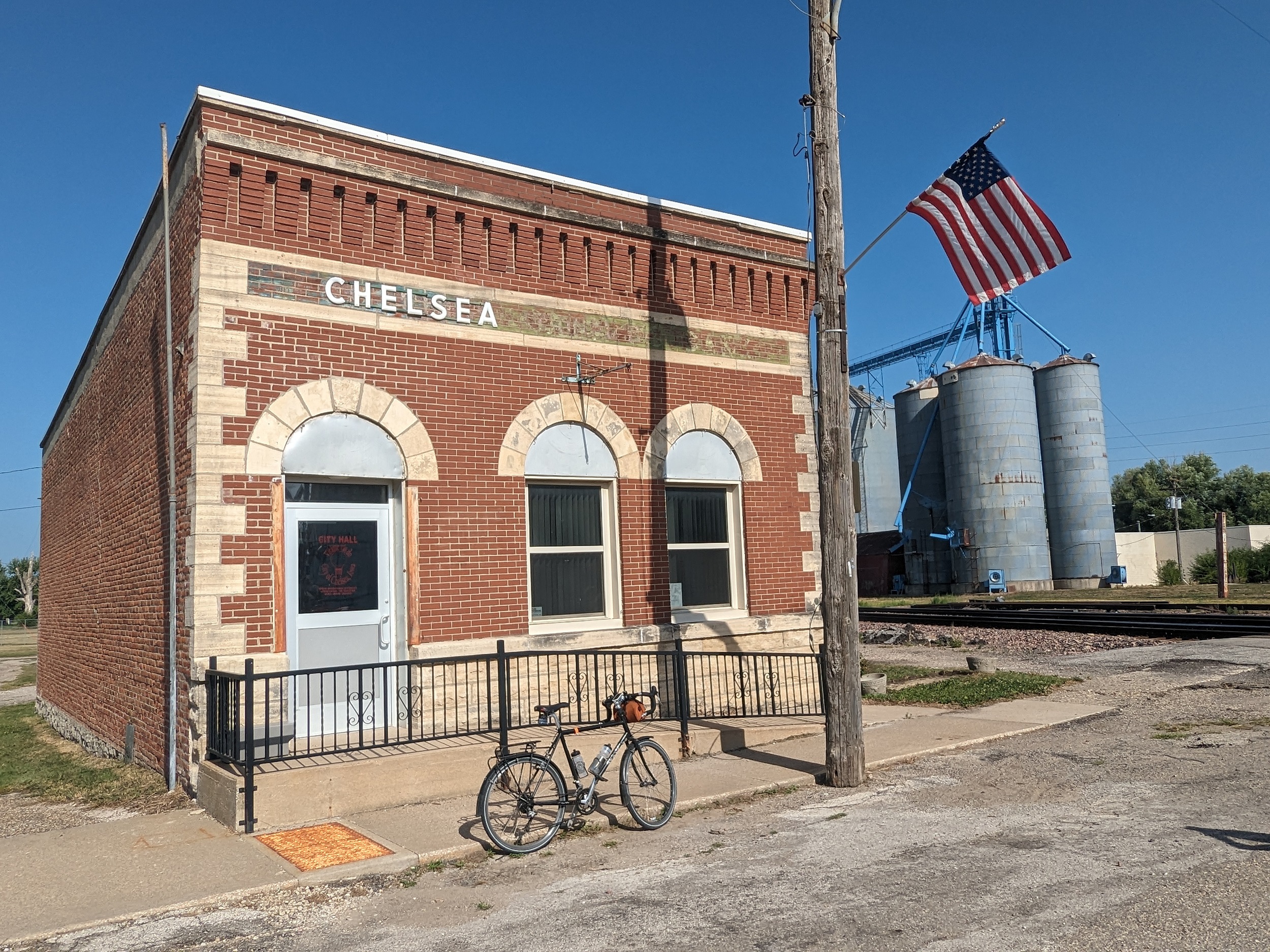 A tour bike standing at the curb in front of a brown brick early 20th Century one story municipal building.