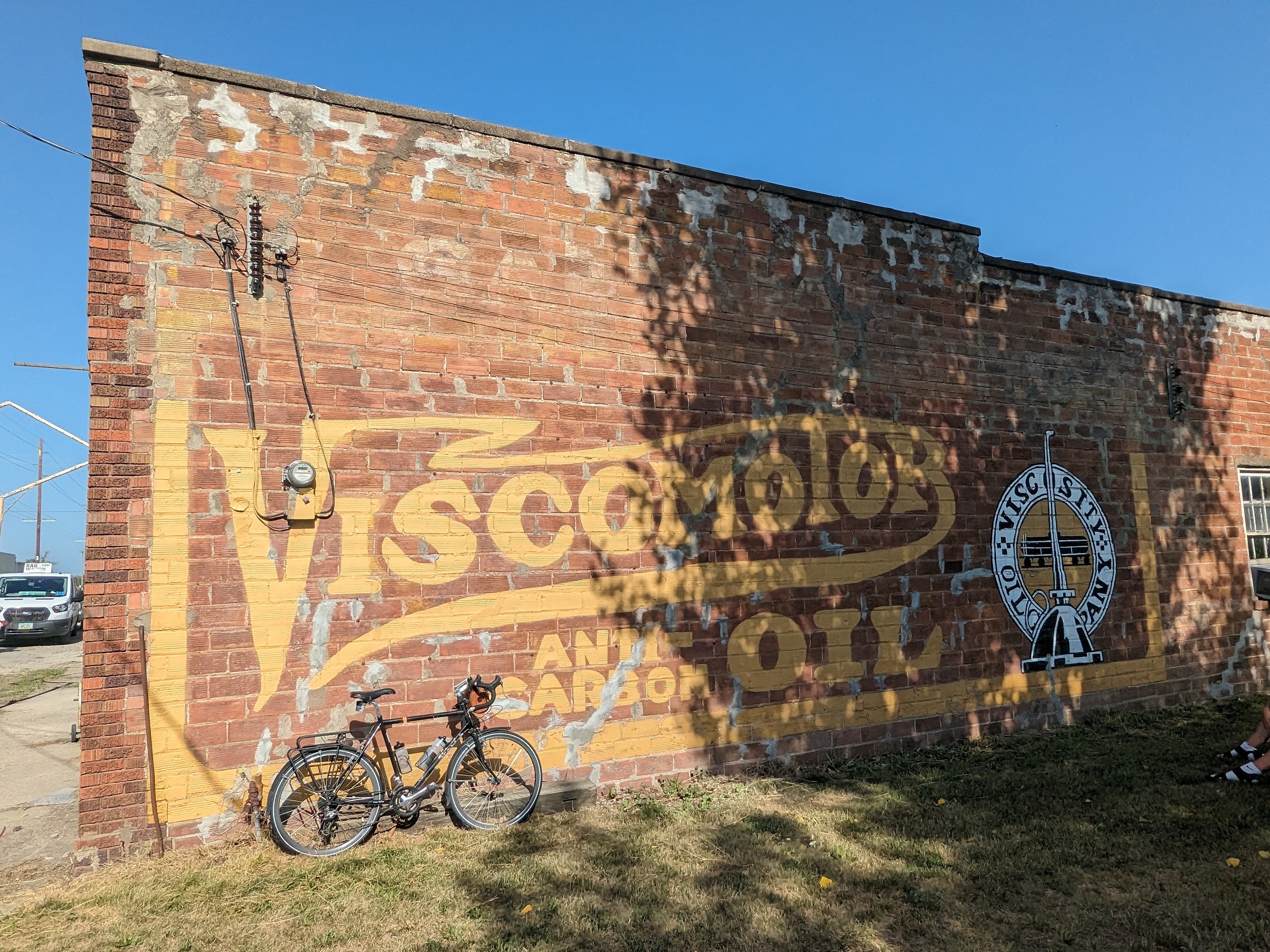 A tour bike leaning on a outside brick wall with a touched up yellow Viscomotor oil ghost sign.