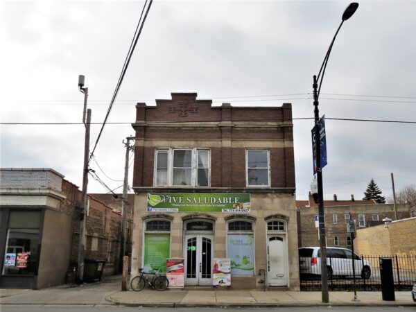 A tour bike leaning at the base of brown brick two story storefront and flats with a Gothic Revival limestone clad first story.