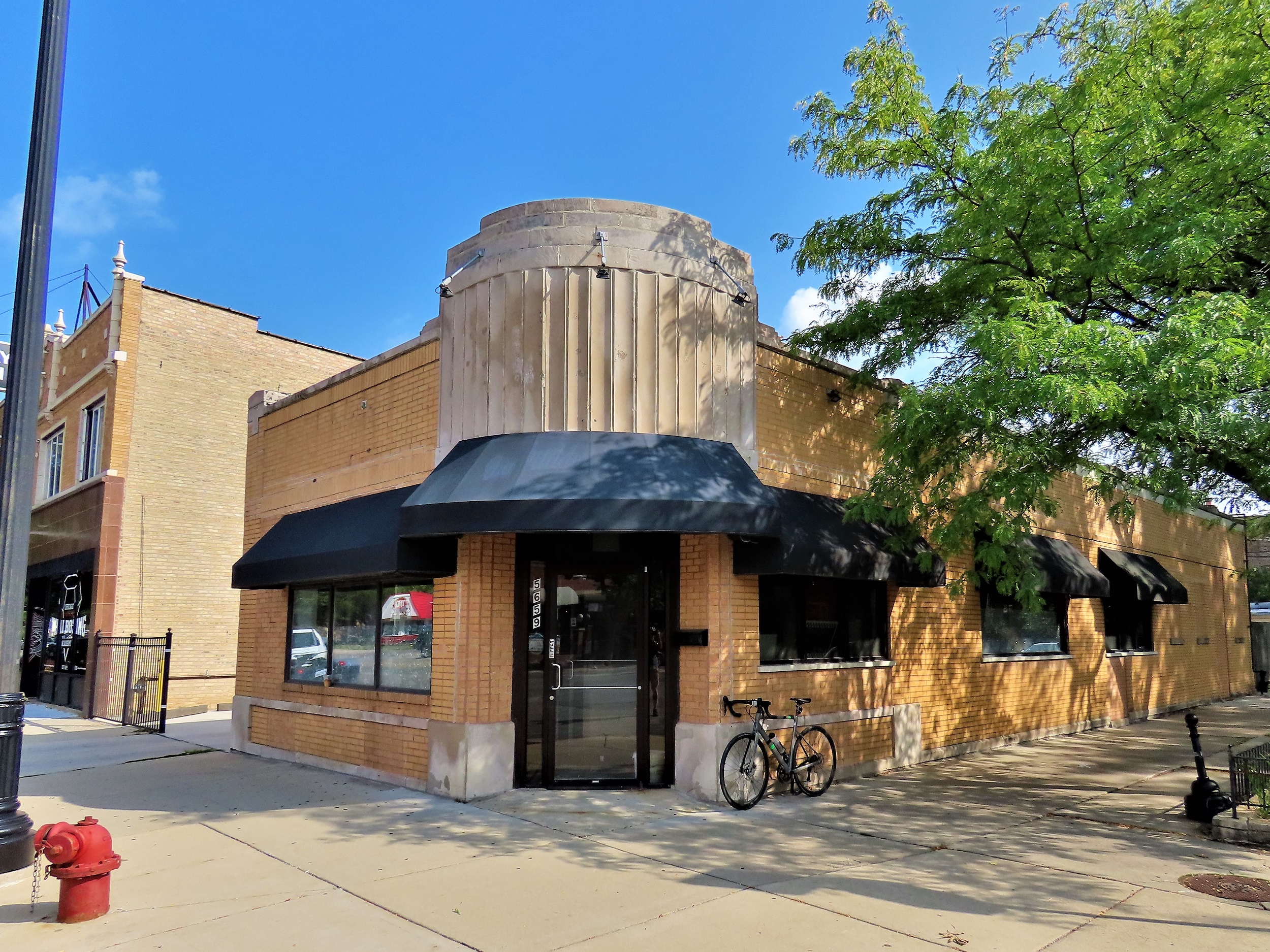 A tour bike leaning next to the corner entrance of a yellow brick one story with a limestone Art Deco second story design above the doorway.