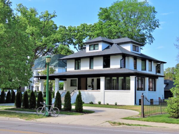 A tour bike standing at front of a three story low hipped roof white painted brick American Four Square residence.