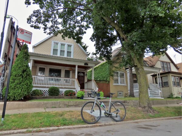 A tour bike standing at front of a two story wood residence with a front porch,