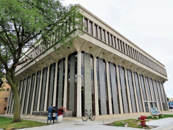 A tour bike leaning at the corner of a five story Mid Century Modern bank that extends at the top like a pedestal with long vertical stripe alternating with grey stone, glass and white concrete.