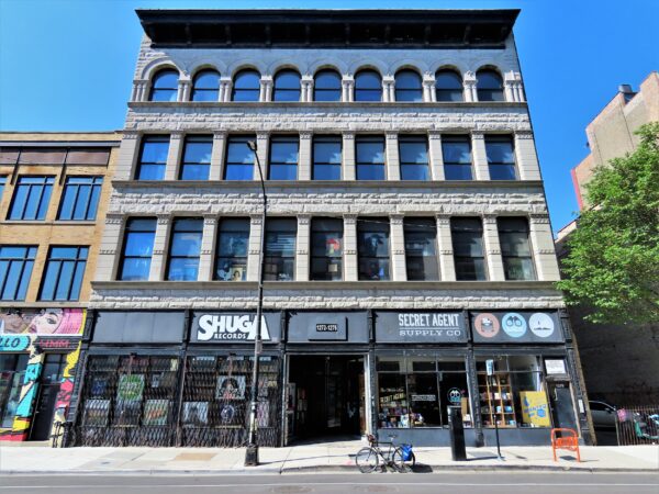 A tour bike standing at the base of a four store limestone late 19th Century department store building with modern tenants and signs.