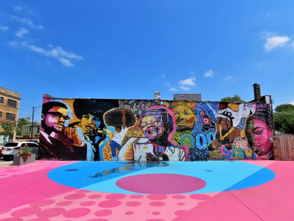 A tour bike leaning on a colorful mural of Black female icons on the other side of a pink and light blue painted basketball court.