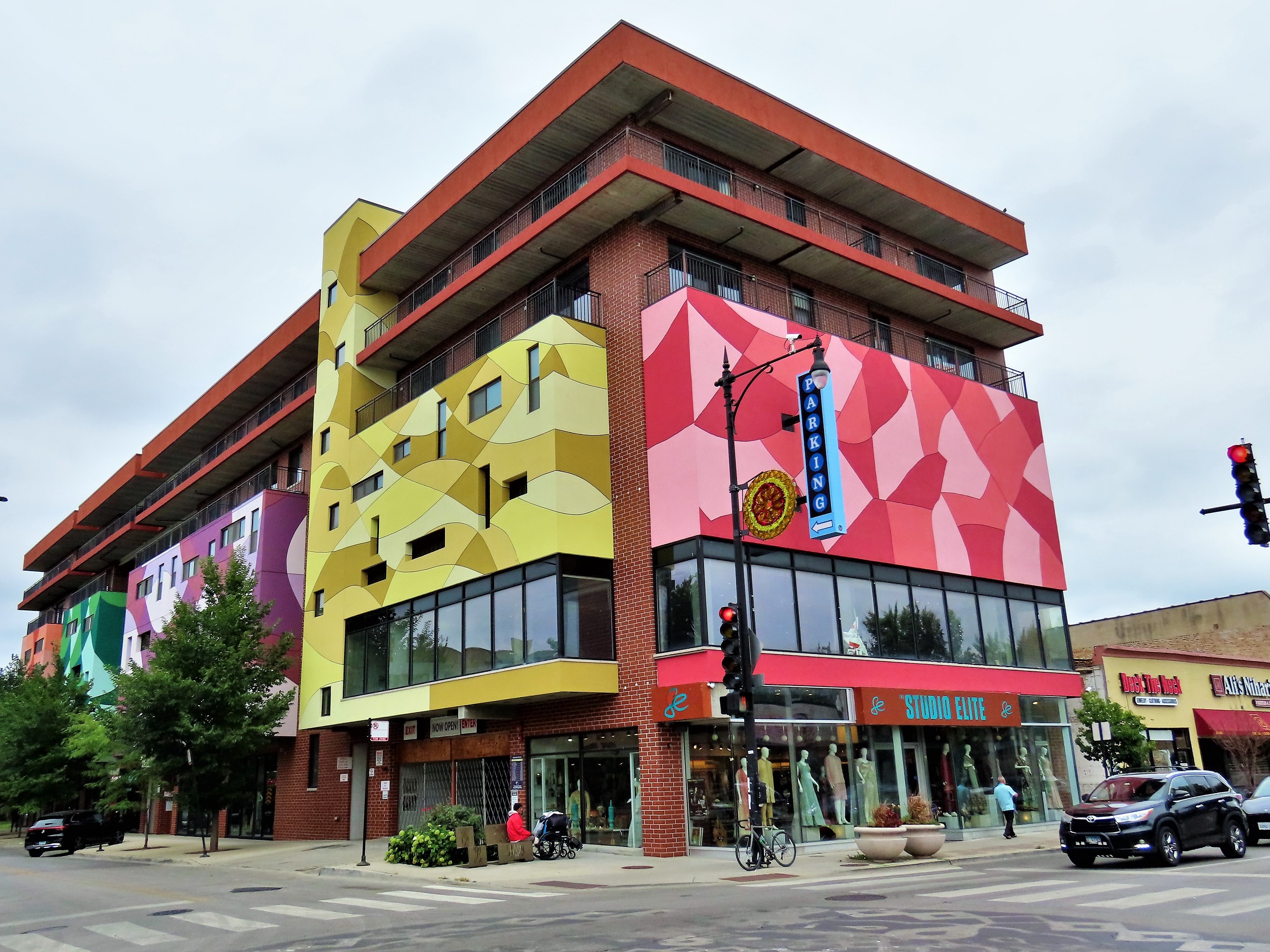 A tour bike leaning on a light post at the corner of a six story double lot flat roof red brick storefront and above parking with colorful geometric murals.