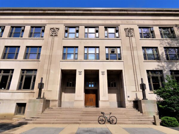 A tour bike standing on the stairs of a limestone educational building with Prairie School design accents.