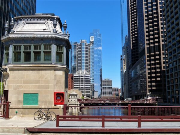 A tour bike leaning on an SEcond Empire bridge minder house with the river extending in the distance between skyscrapers.