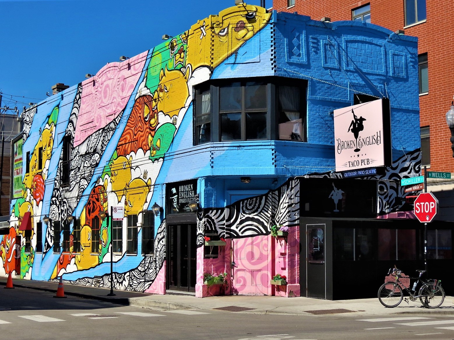 A tour bike standing at front of a two story brick corner restaurant covered in a colorful cartoon bear themed mural.