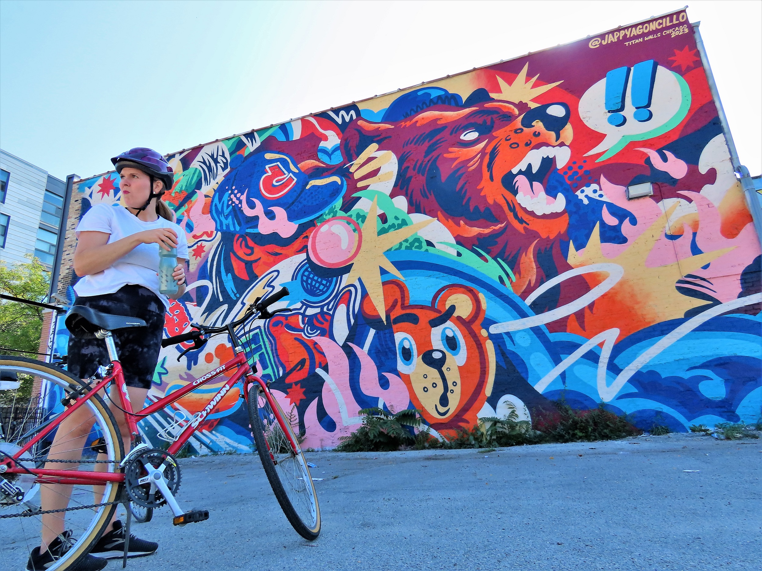 A CBA bike tour rider standing in front of a large format blue and orange base Chicago sports themed mural.