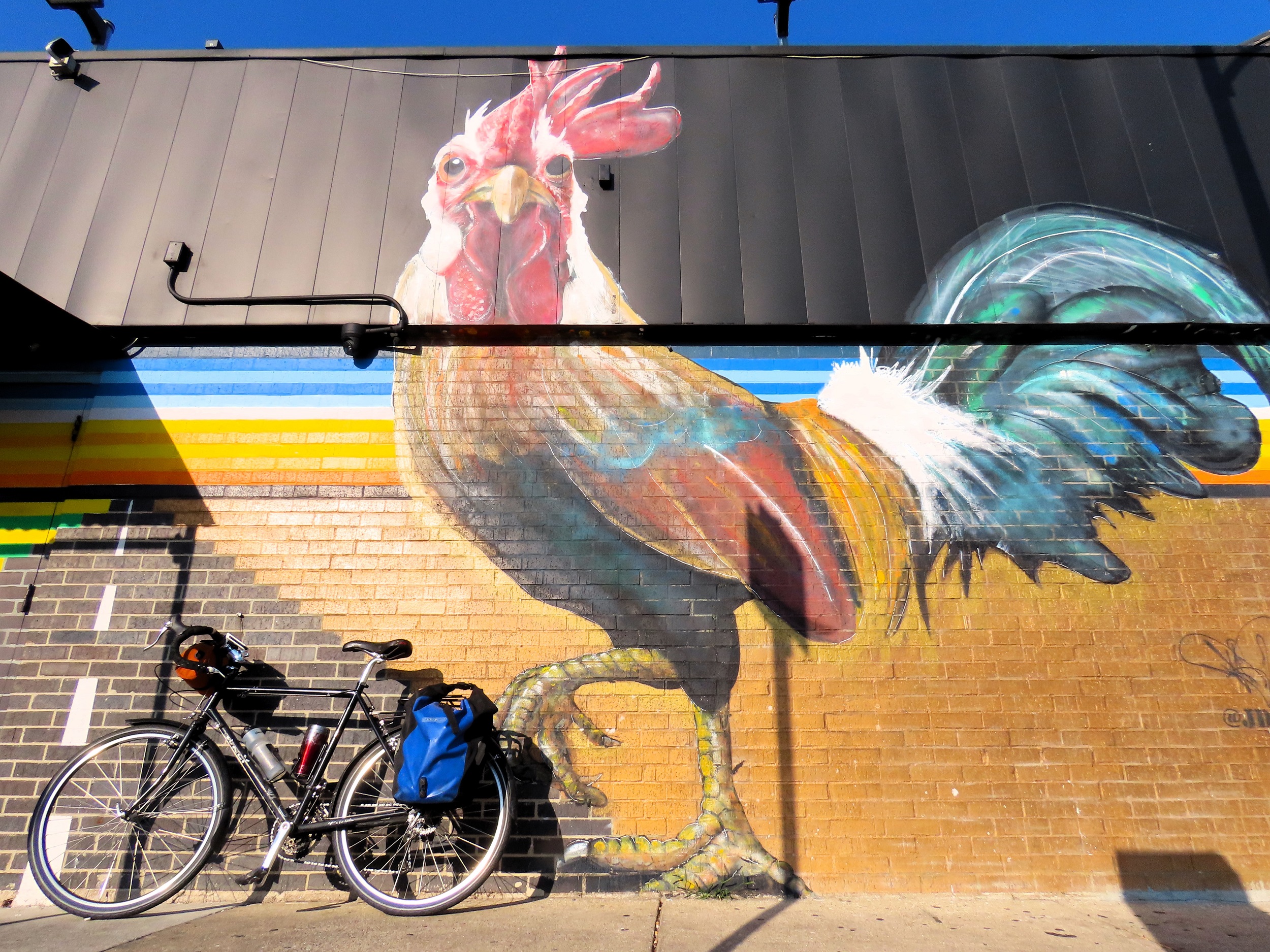 A tour bike leaning on a wall with a large chicken mural looking directly at the camera.