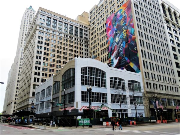 A tour bike below skyscrapers, one covered with a colorful mural of Muddy Waters.