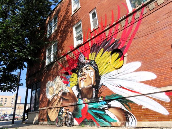 A tour bike leaning on a mural of a Central American First Nation man with a headdress of feathers offering a shell with both hands.