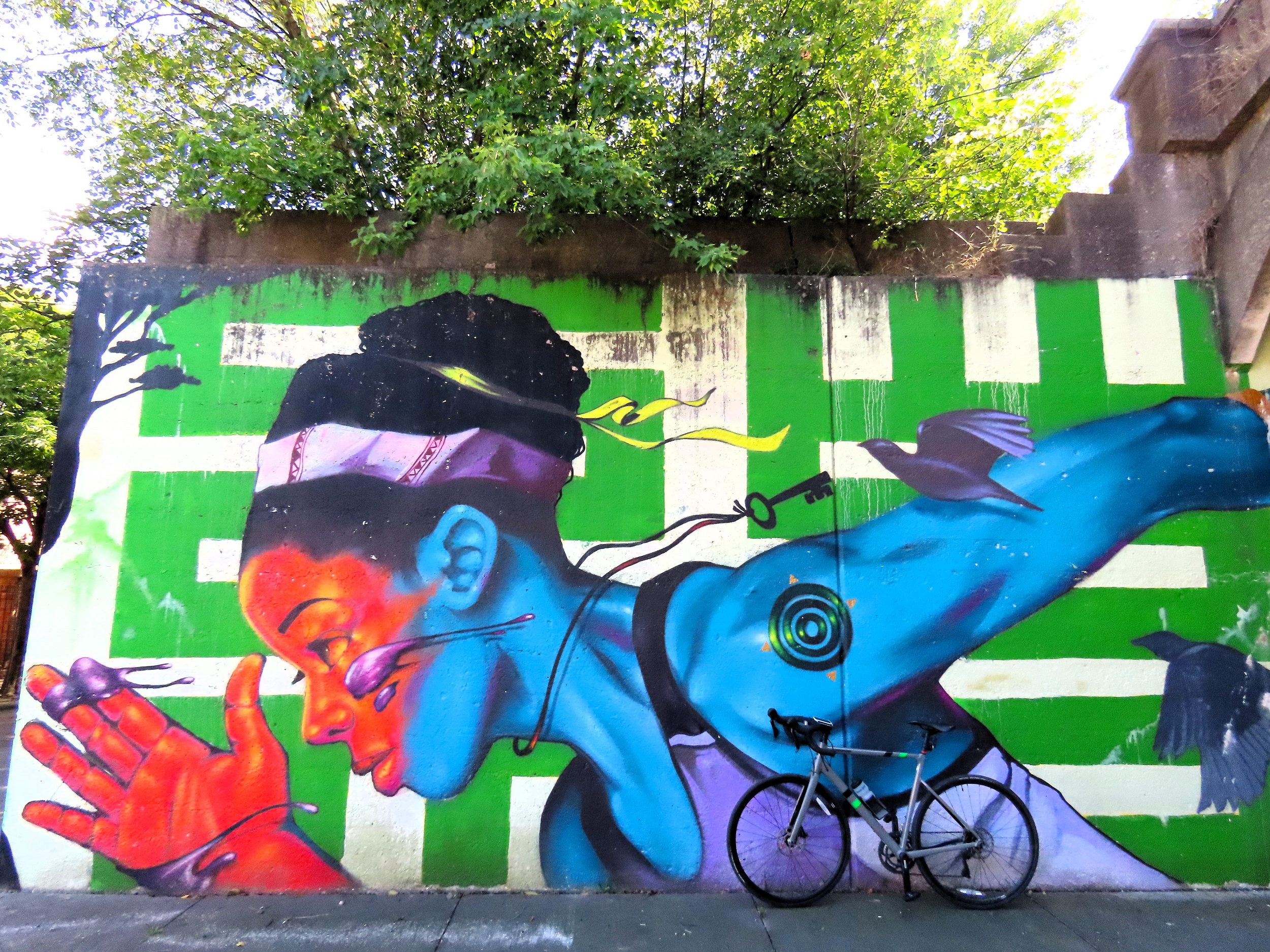 A tour bike leaning on a bright colored mural of the upper half of a Black woman sprinting.