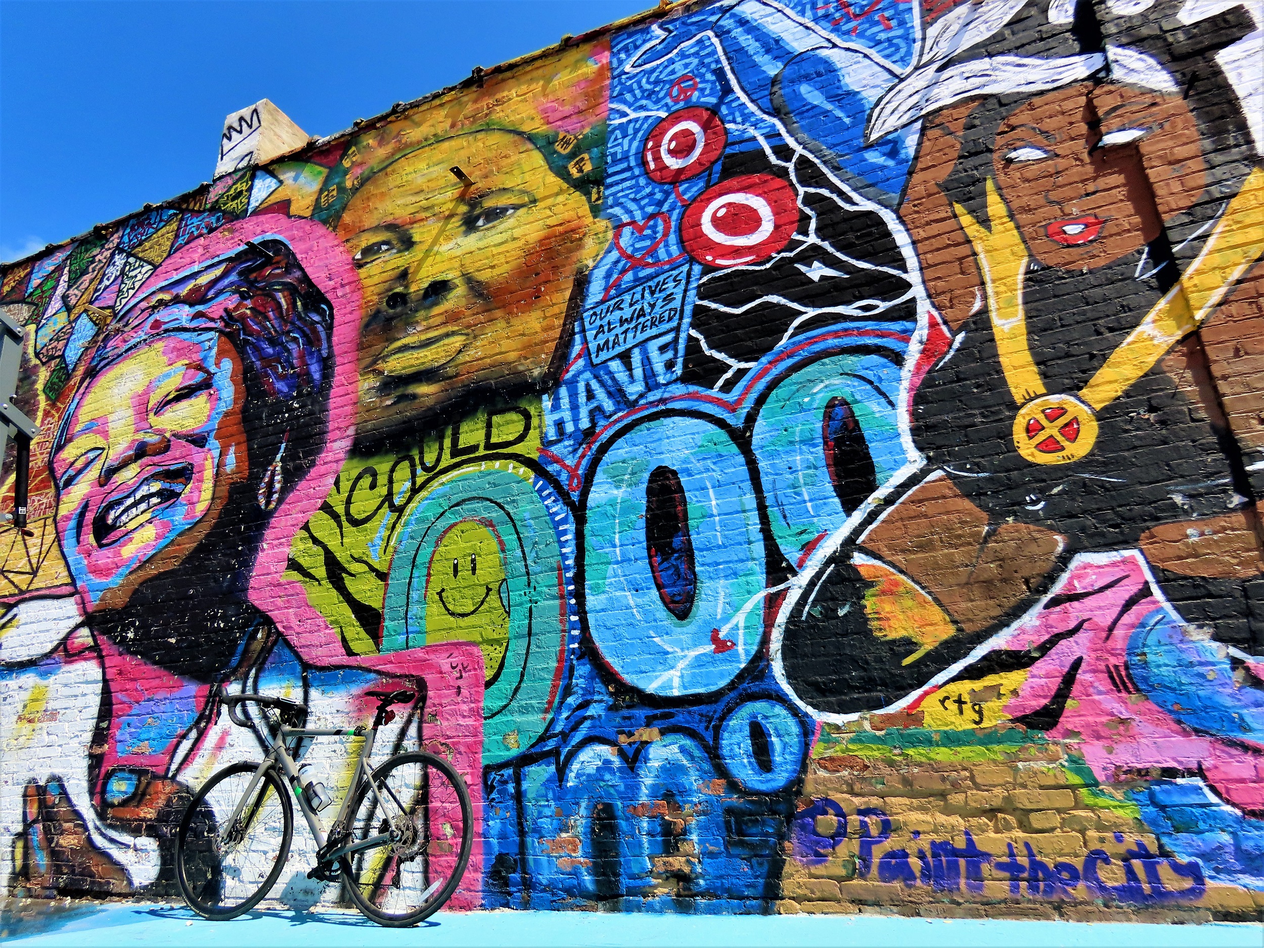 a tour bike leaning on a mural depicting Black female icons real (Harriet Tubman) and fictional (Storm from the X-Men)