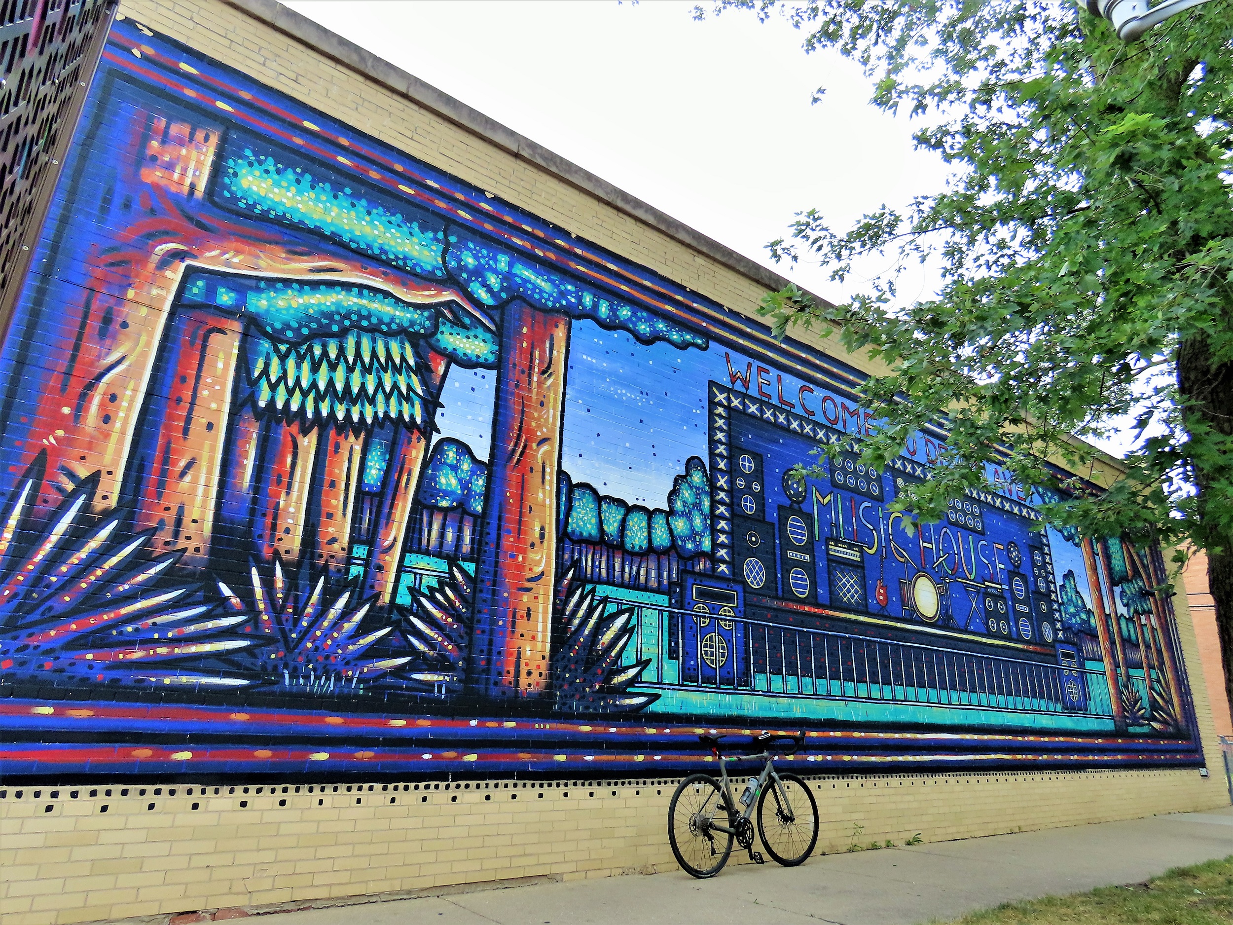 A tour bike leaning underneath a blue based cartoon pointillist like stage among the woods mural.