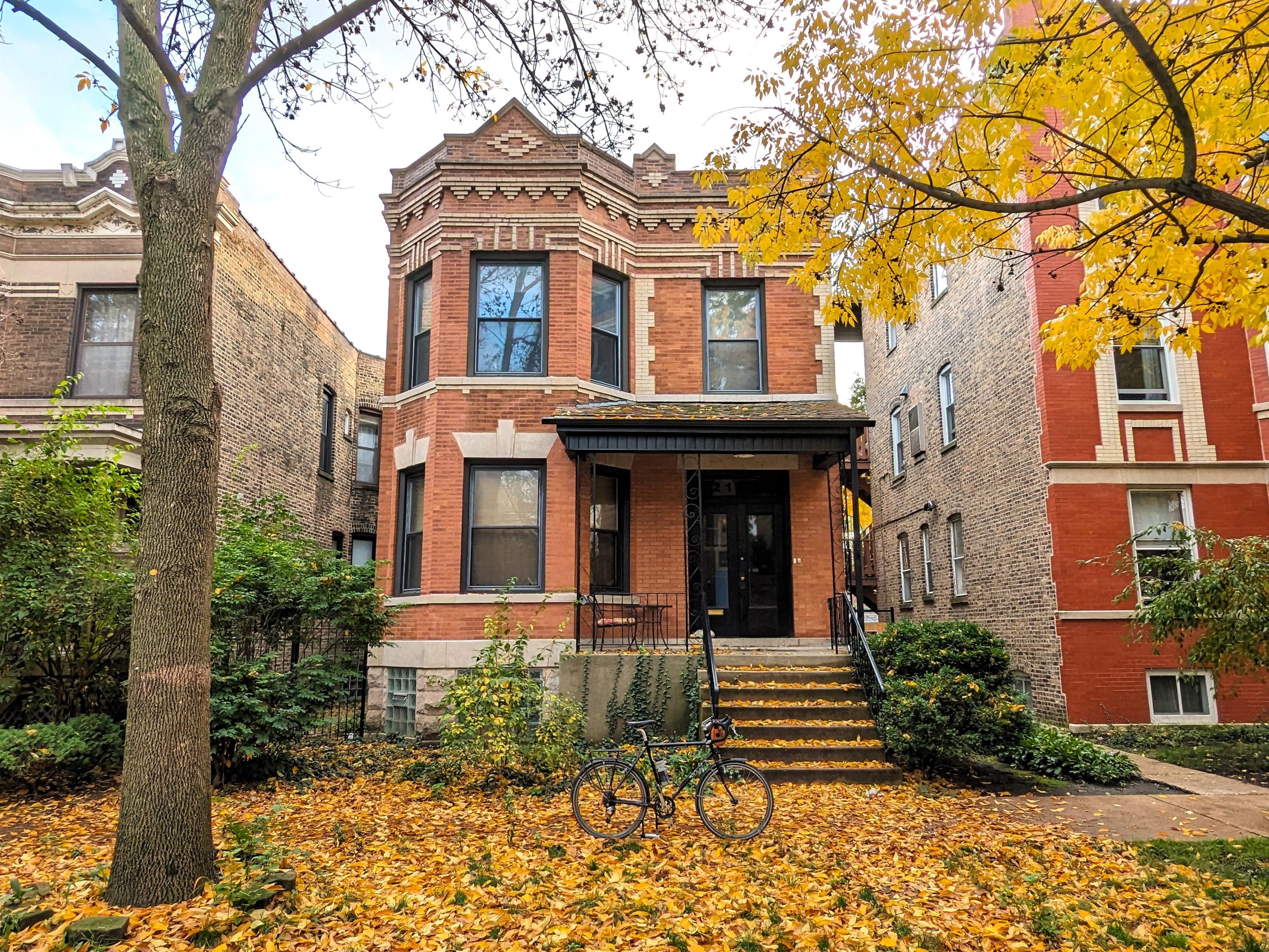 A tour bicycle standing in front of an early 1900s brown brick two flat with tan brick designs among Fall color.