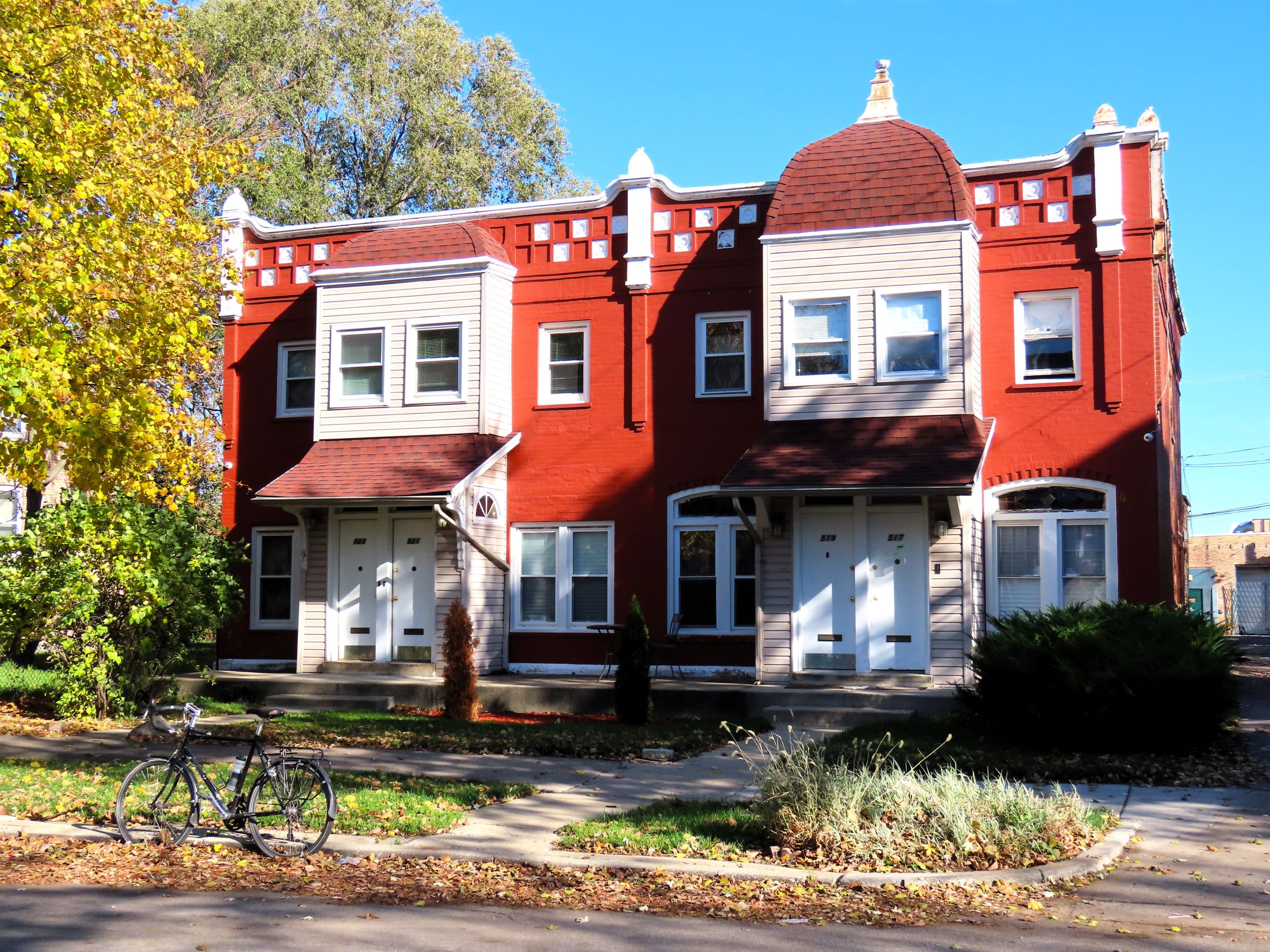 a tour bicycle standing at front of a red brick Queen Anne two story mini rowhouse with four units,