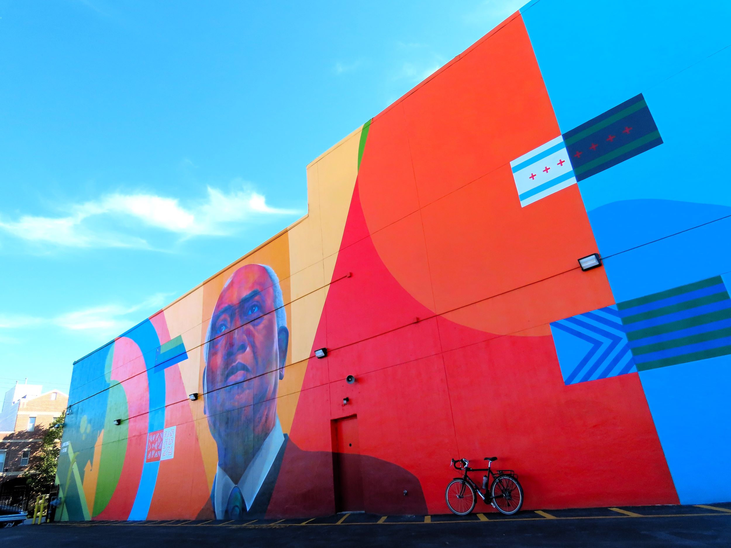 A tour bicycle leaning at the base of a large bright geometric shape mural with a portrait of congressman Danny Davis.