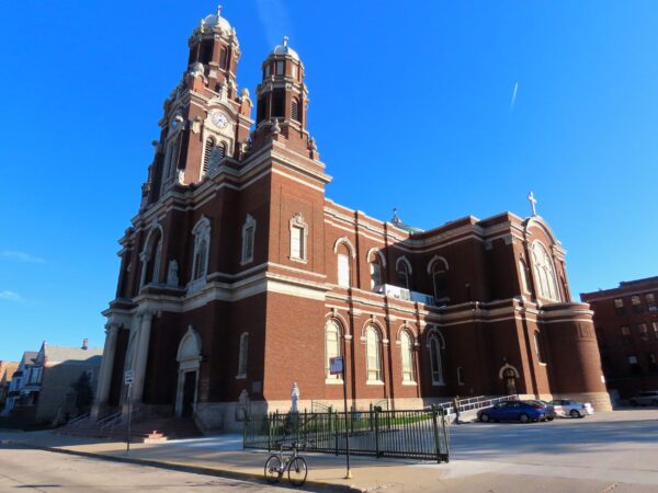 A tour bicycle standing at the bottom of a very large brown brick Baroque Revival style church.