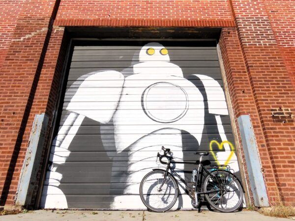 A tour bicycle leaning on a roll up door with a Giant Robot mural on it.