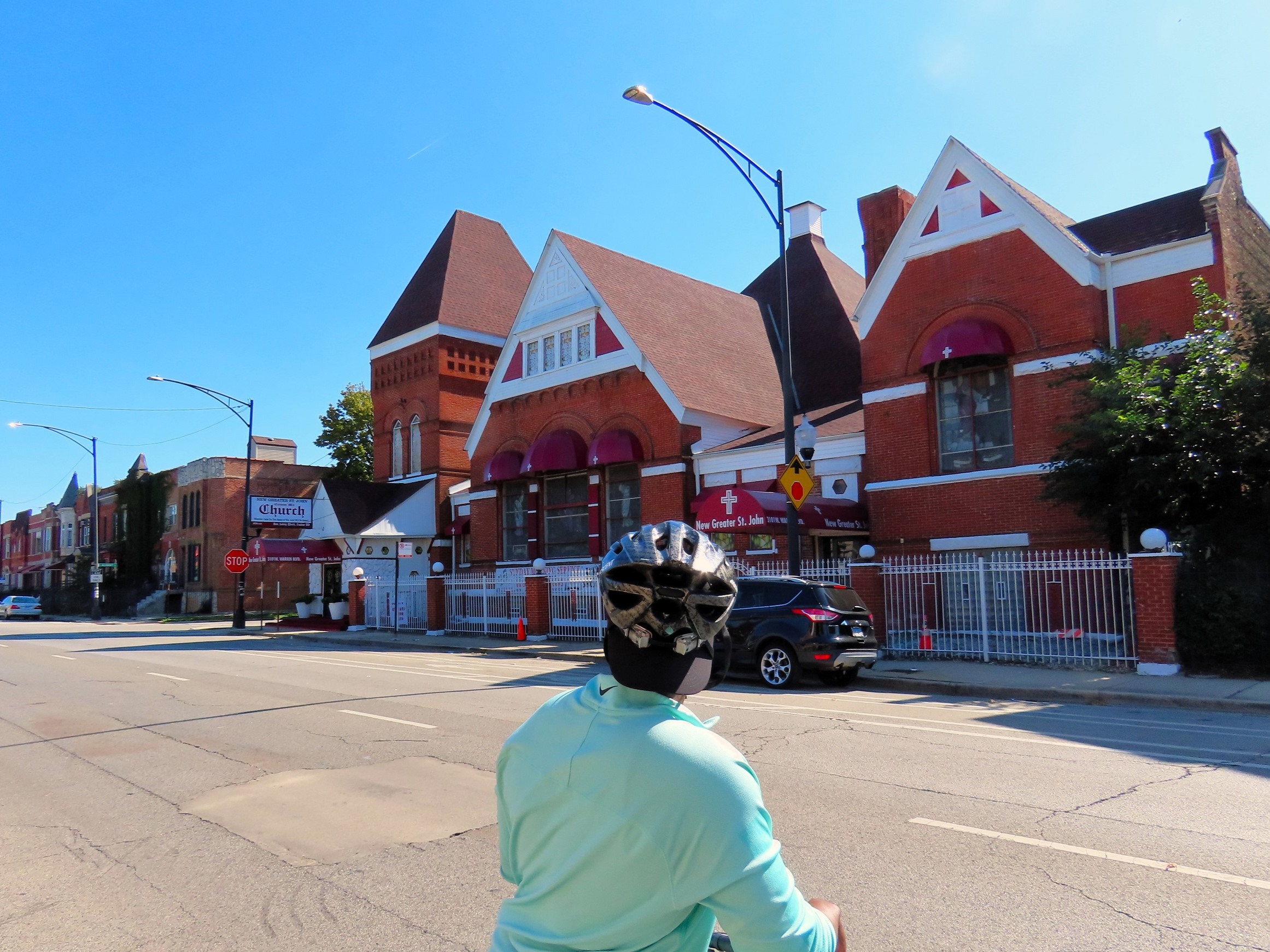 A CBA rider seen from behind loking at a red brick and white wood one story triple lot wide 1890s church.