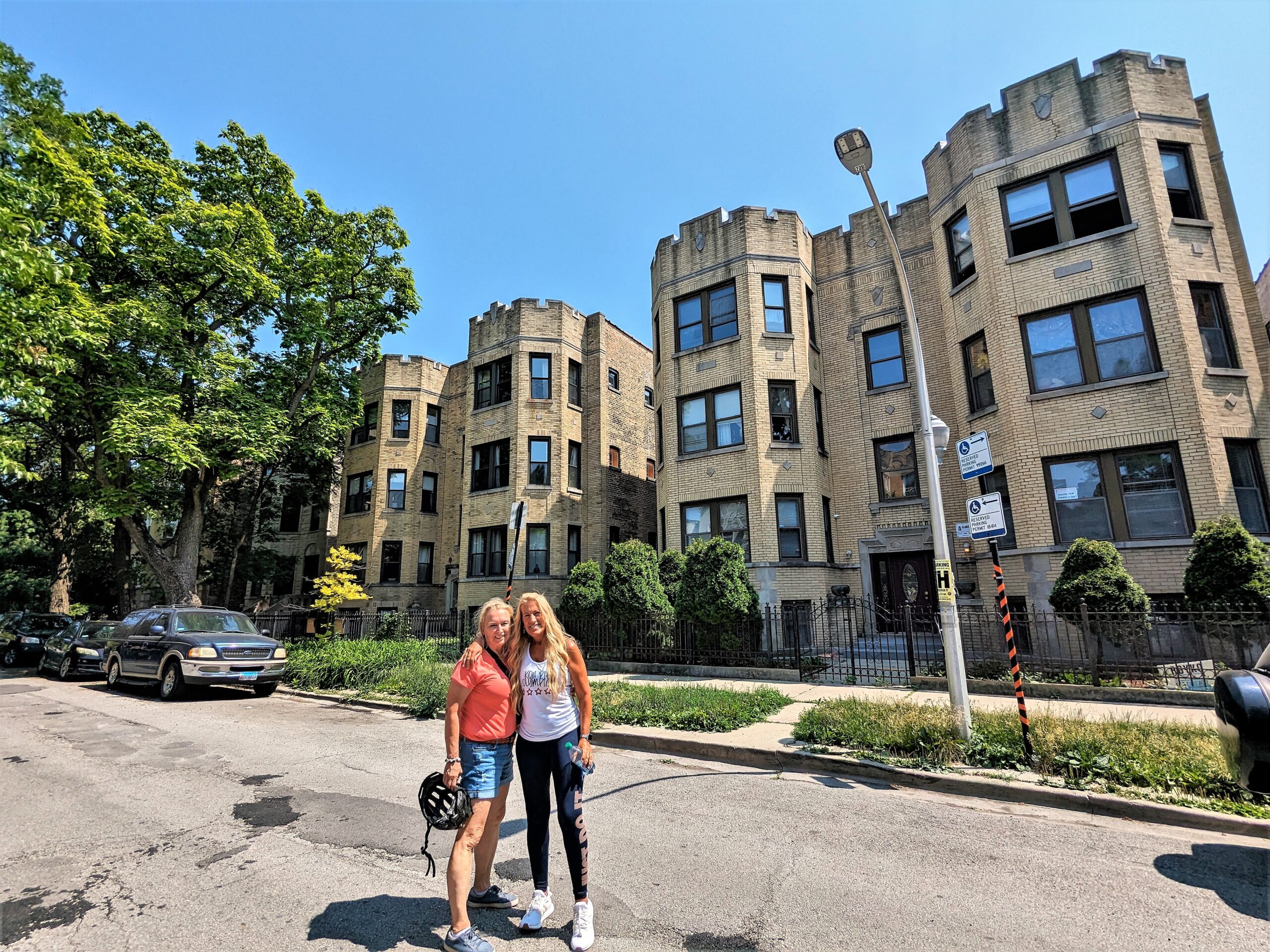 Two CBA riders smiling in front of a yellow brick three story 1920s apartment building.
