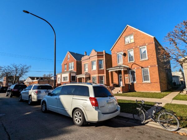 A tour bicycle standing in front of an early 1900s two story red brick single family home.