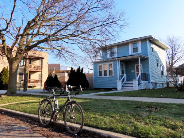 A tour bicycle standing at front of a pale blue early 1900 two story wood single family home.