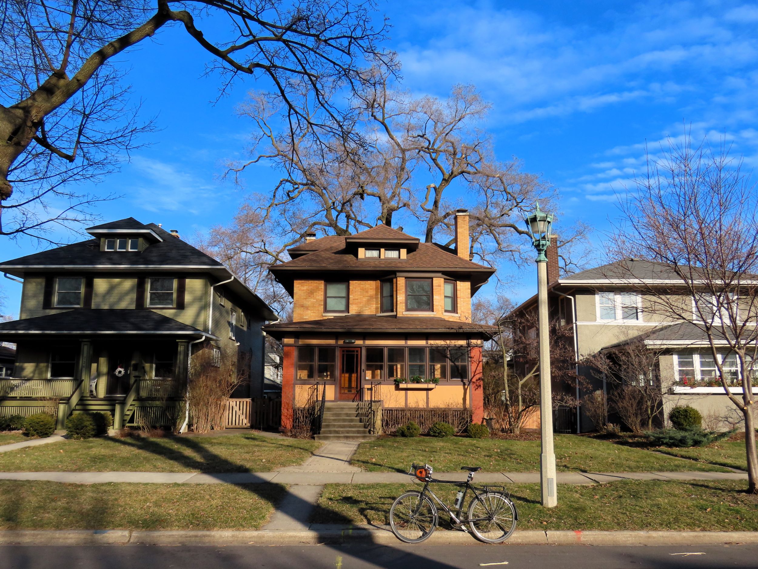 A tour bicycle standing at front of a n early 1900s tan brick American Four Square house with similar neighbors on either side.