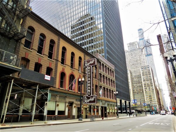 A tour bicycle standing at front of a block of 1880s Italianate three story building of different colors with a modern skyscraper in the distance.
