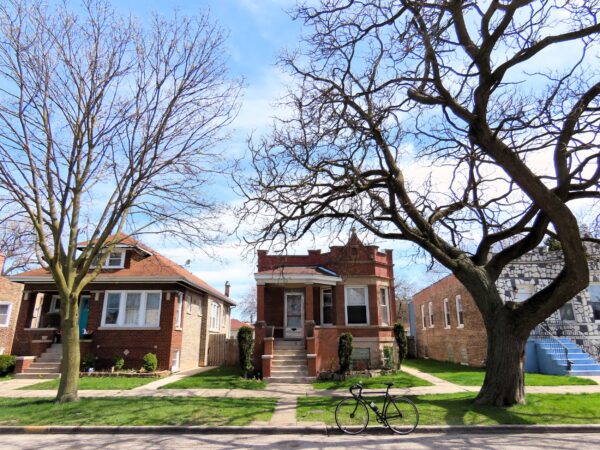 A tour bicycle standing at front of an early 1900s flat roof red brick one story single family home.