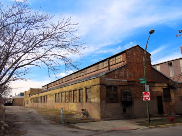 A tour bicycle leaning on the side of an early 1900s one story corner industrial shop building with the shape of a long cartoon church.