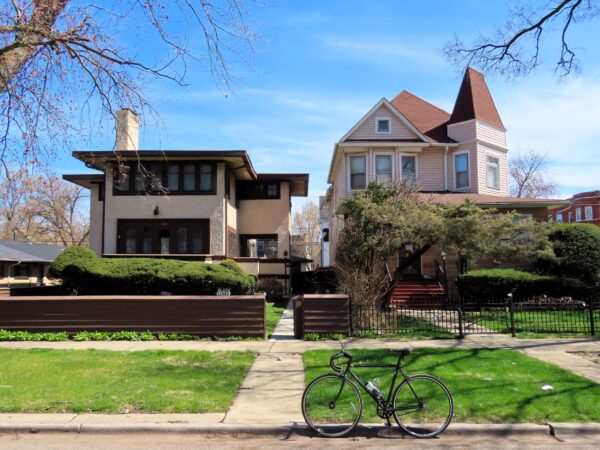 A tour bicycle standing in front of an early 1900s Queen Anne two story wood single family home on the right and a two story Prairie School home at left.
