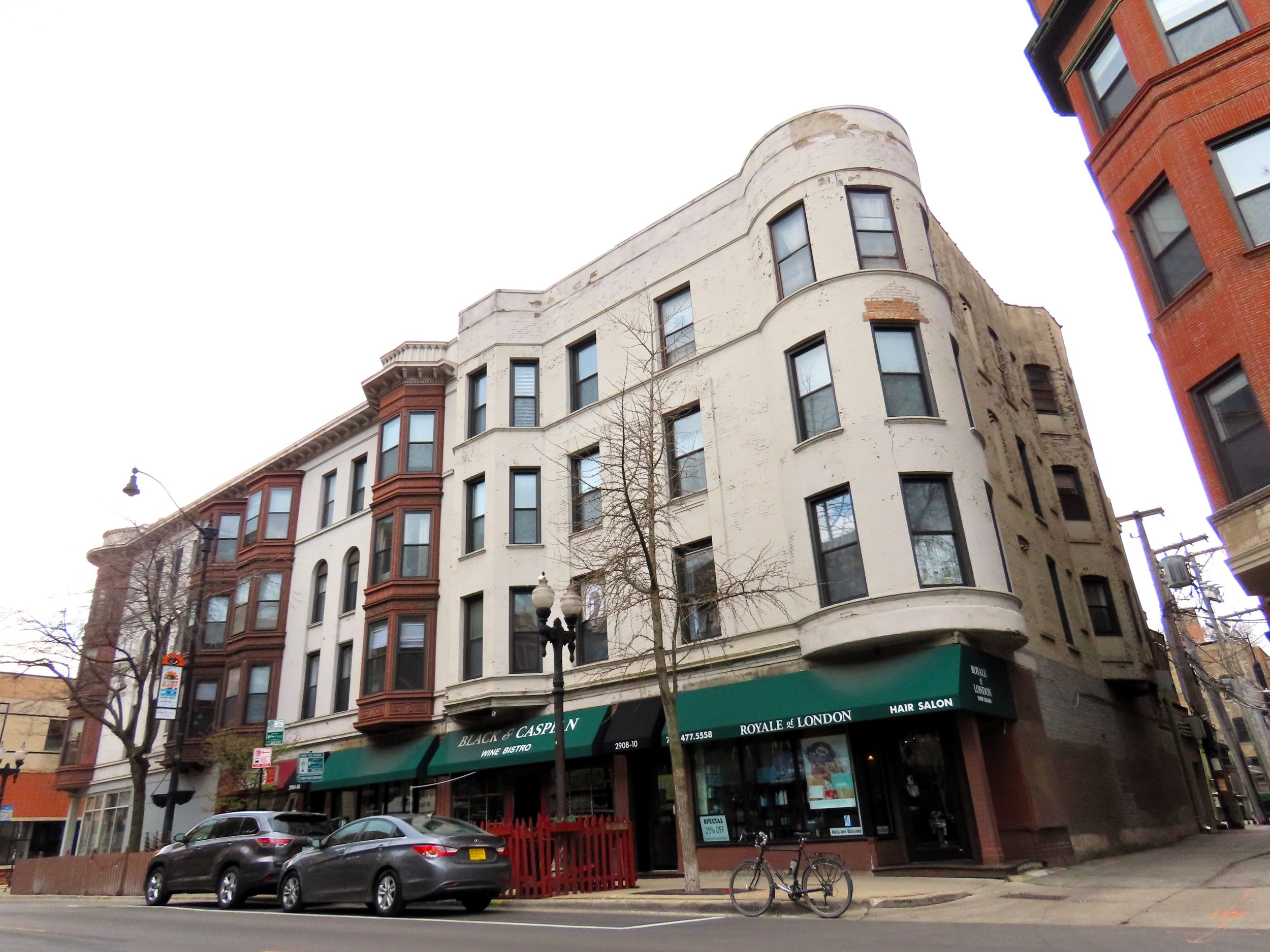 A tour bicycle standing at the corner of a late 1800s four story storefront and flats with white painted brick a rounded corner bays.