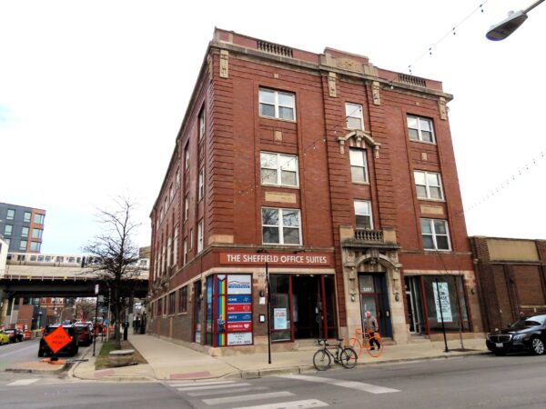 A tour bicycle standing at front of an early 1900s brown brick three story social club hall.