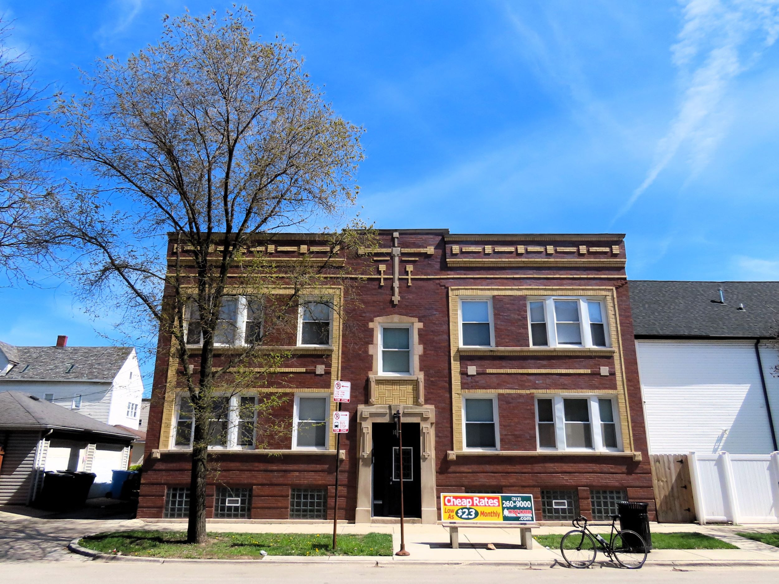 A tour bicycle standing at front of an early 1900s brown brick double lot two story apartment building with an ornate central limestone entry and a yellow brick accented façade.