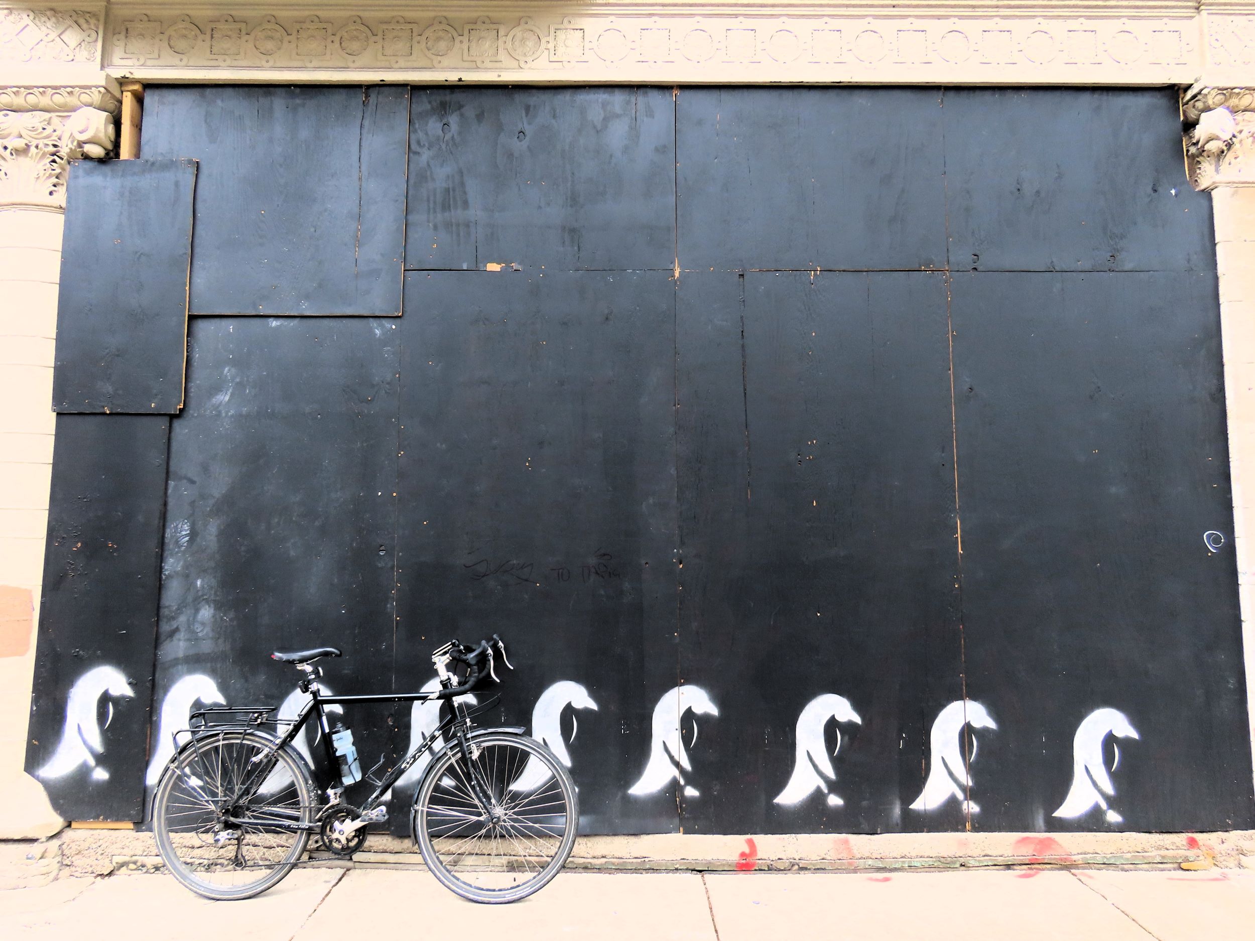 A tour bicycle leaning at right on a black painted board with a single row of white stenciled penguins along the bottom