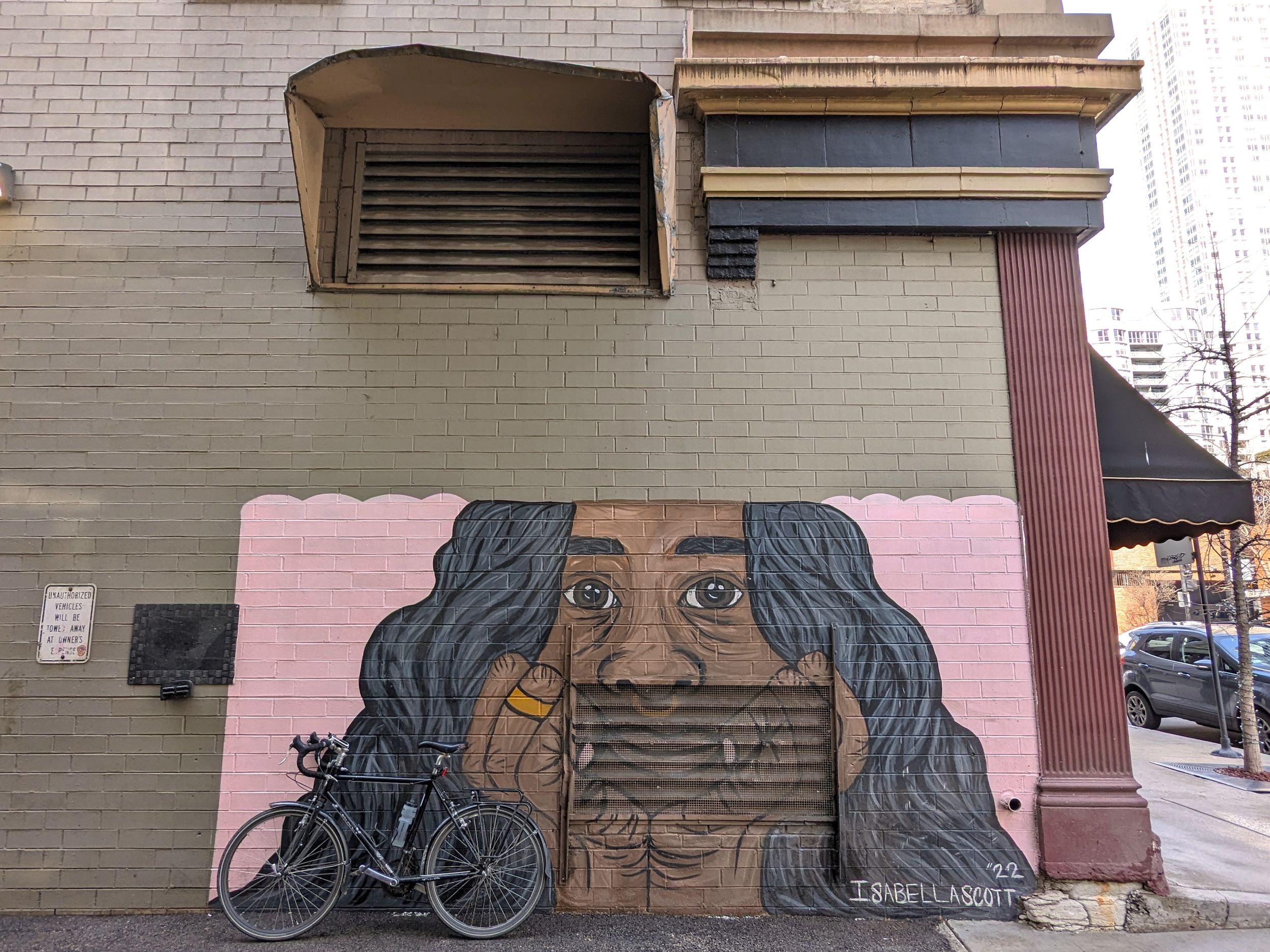 A tour bicycle is leaning on an alley mural of a smiling long wavy haired cartoon Black girl looking at the viewer with her face resting in her hands.
