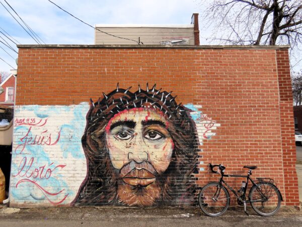 A tour bicycle leaning at right on a restored brick wall with a mural of Jesus remaining on the older part