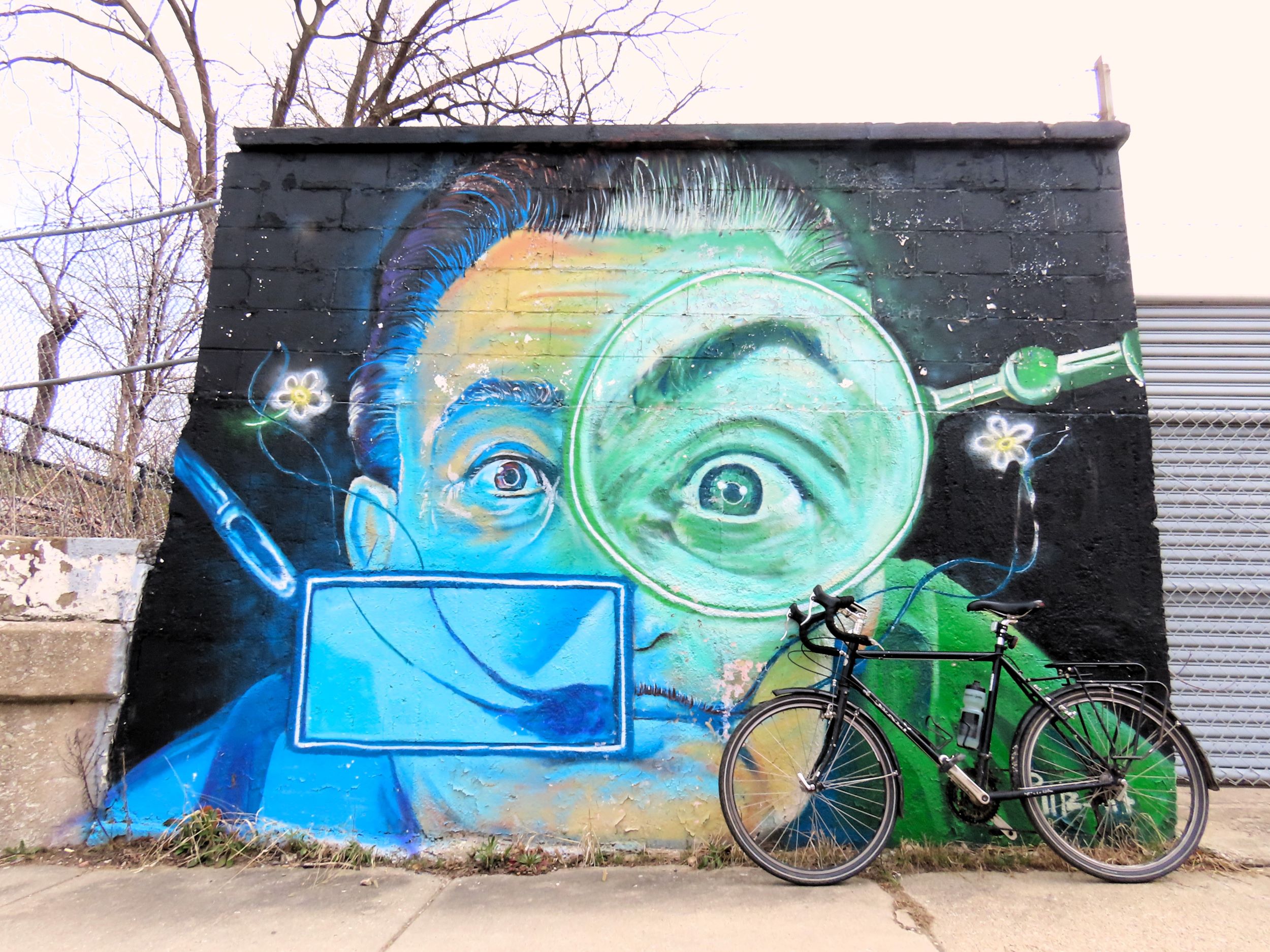 A tour bicycle leaning at right on a bright colored mural of Salavador Dali looking at the viewer.