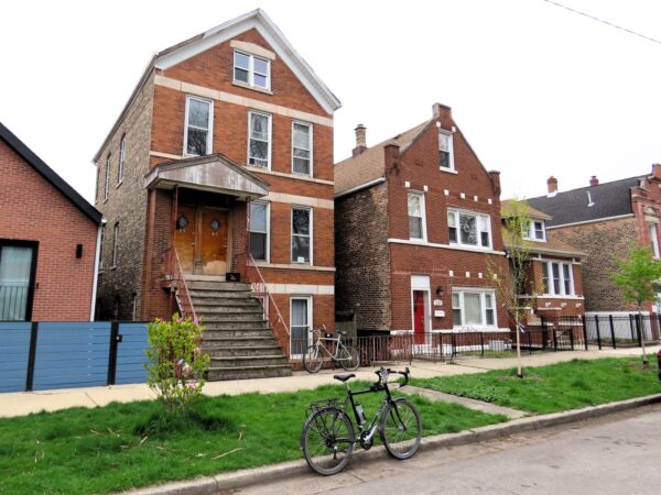 A tour bicycle standing in front of two late 1800s raised two and half story residences.
