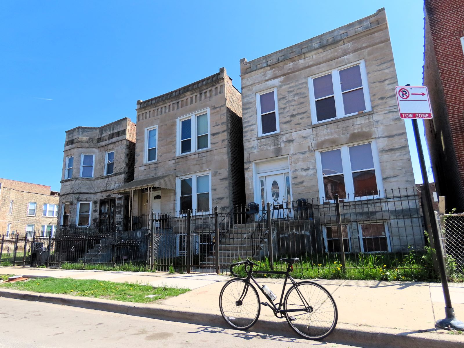 A tour bicycle standing in front of three early 1900s greystone 2 flats.