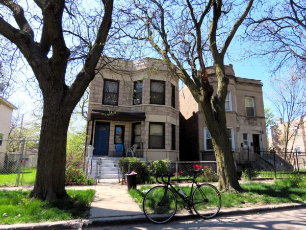 A tour bicycle standing in front of two early 1900s two story greystone single family homes.