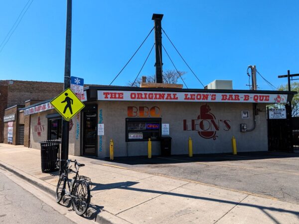 A tour bicycle leaning on the curb in front of a mid century one story restaurant, Leon’s BBQ.