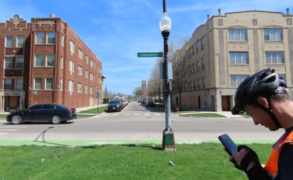 A CBA rider looking at their phone as we can see the two Sears Towers of Chicago through a gap between two 1920s apartment buildings.