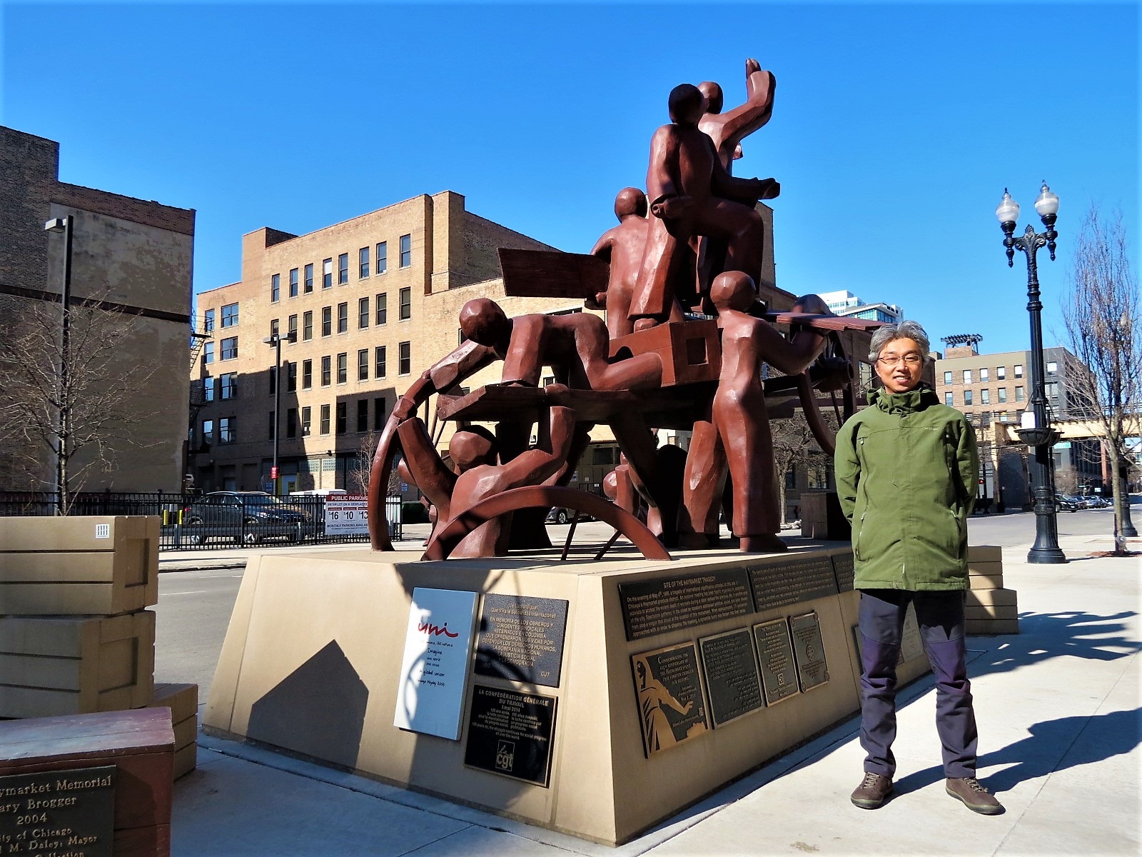 A CBA rider standing next to a copper color sculpture of human like figures standing on a two wheeled cart.