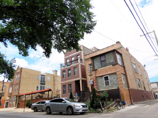 A tour bicycle standing on a city street in front of an early 1900s squared brown brick two flat with glass block filled sunrooms.