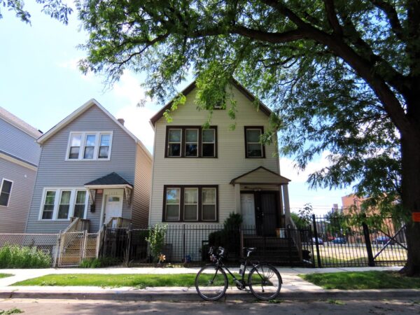 A tour bicycle standing in front of two late 1800s two story wood framed homes shaded by a tree.